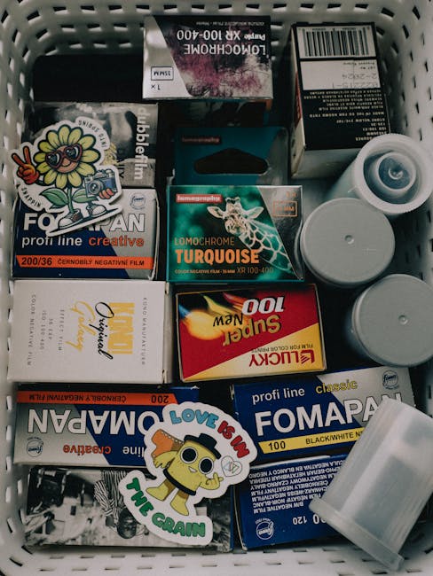 Inside a plastic storage box filled with various items prepared for home relocation, including several small cardboard boxes of photographic paper and film with labels indicating different brands and 